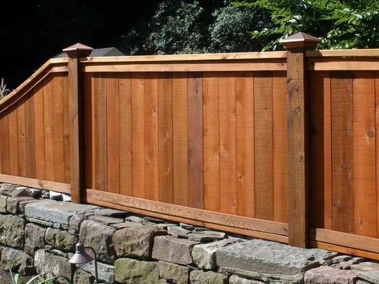 Wooden fence with copper-topped posts atop a stone wall, in a sunny outdoor setting.