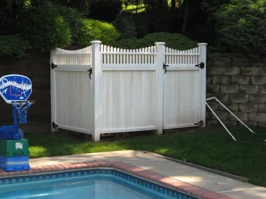 White outdoor shower enclosure next to a swimming pool, with a basketball hoop.