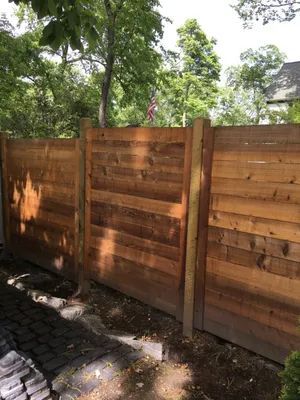 Wooden horizontal slat fence in a yard, with green trees in the background.
