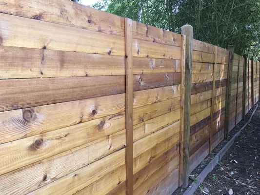 Wooden horizontal slat fence. Light brown wood, upright posts, outdoor setting.