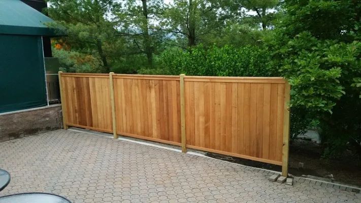 Wooden privacy fence on a brick patio with greenery in the background.