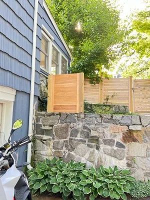 Wooden box on stone wall near blue-sided building with a fence and lush greenery.
