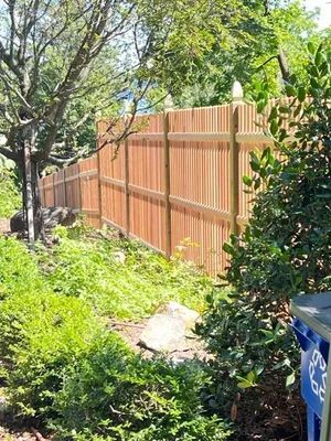 Wooden fence in a garden setting, surrounded by lush green foliage and trees.