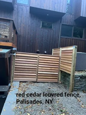 Red cedar louvered fence in Palisades, NY. It is brown and installed against a dark wood building.
