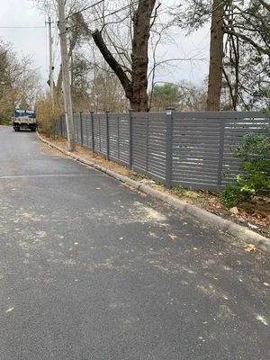 Grey horizontal slat fence along a road. A utility truck is in the distance.