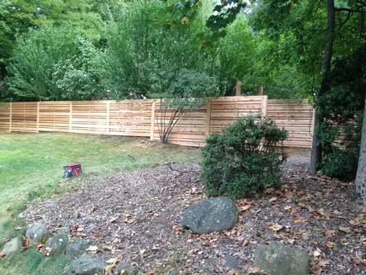 Wooden horizontal slat fence in a backyard, with trees in the background.