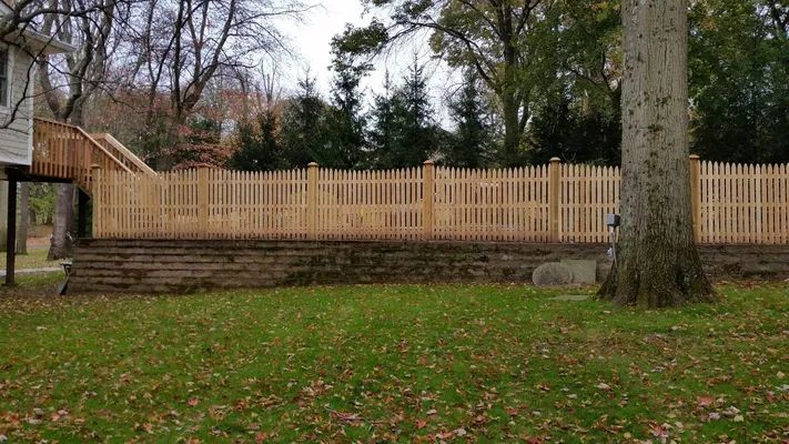 Wooden picket fence on a brick foundation, surrounded by grass and trees.