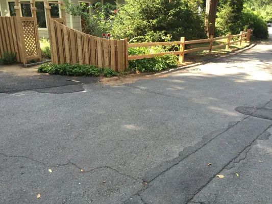Asphalt road with a wooden fence and a house in the background.