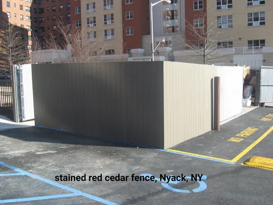 Stained red cedar fence in Nyack, NY, enclosing an area. Adjacent to asphalt with
