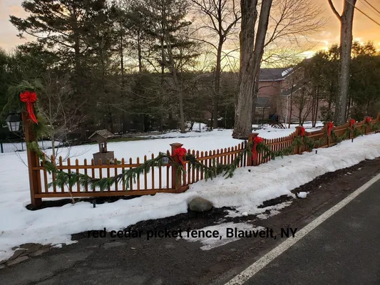 Cedar picket fence decorated for Christmas with snow and trees in Blauvelt, NY.