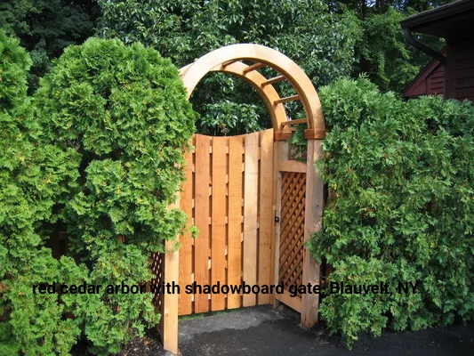 Redwood arbor with shadowboard gate in a garden surrounded by green bushes.