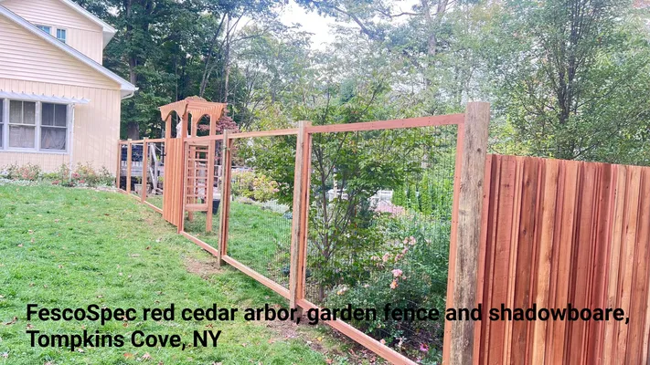Red cedar arbor and fence in Tompkins Cove, NY, bordering a lawn next to a light-colored house.