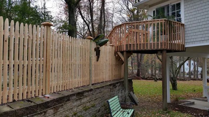 Wooden picket fence alongside a retaining wall with a small raised deck attached to a house.