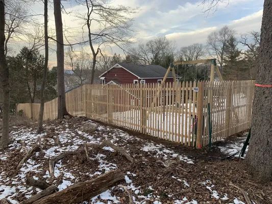 Wooden fence surrounding a backyard with a swing set, house, and snowy ground.