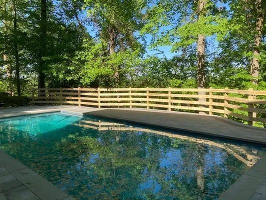 Swimming pool with turquoise water, wooden fence, and trees in the background.