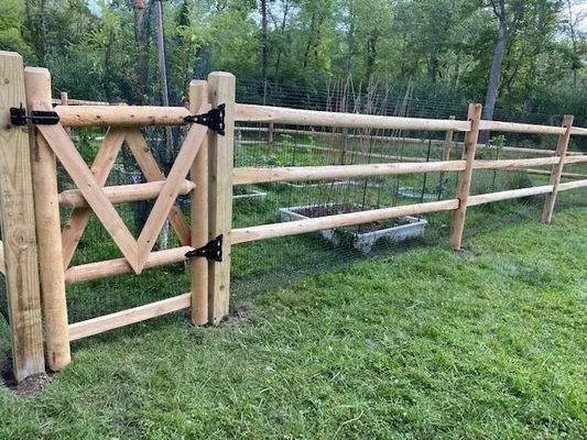 Wooden gate and split-rail fence in a grassy yard, with a flower box visible.
