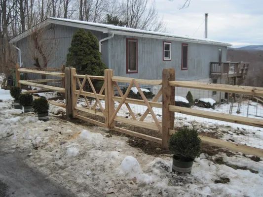 Wooden fence with decorative gate in front of a house, snowy ground.