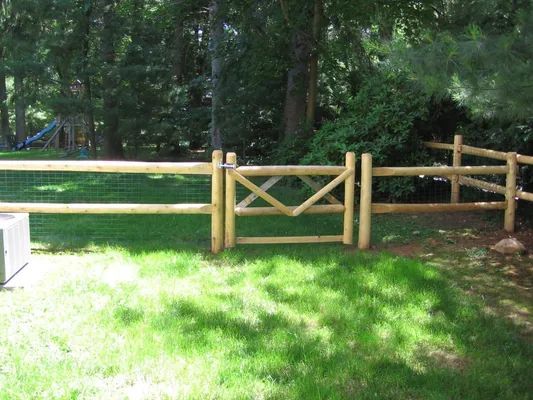 Wooden fence with gate in a grassy yard, trees in background.