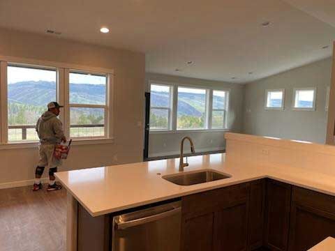 A person in a grey sweatshirt painting a room with a mountain view through the windows. Kitchen counter in foreground.
