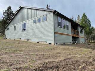 Two-story house with gray siding and a brown roof on a grassy hill.