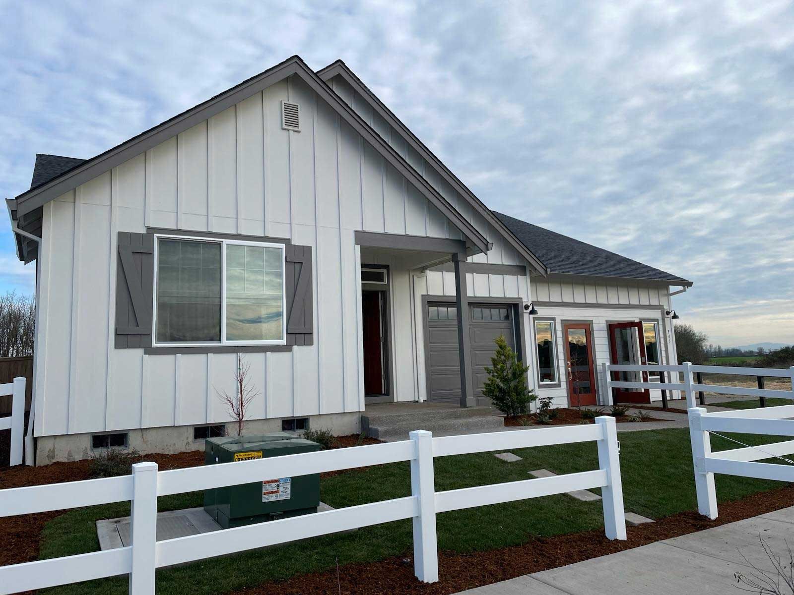 White farmhouse-style home with gray accents, shutters, and fence under a cloudy sky.