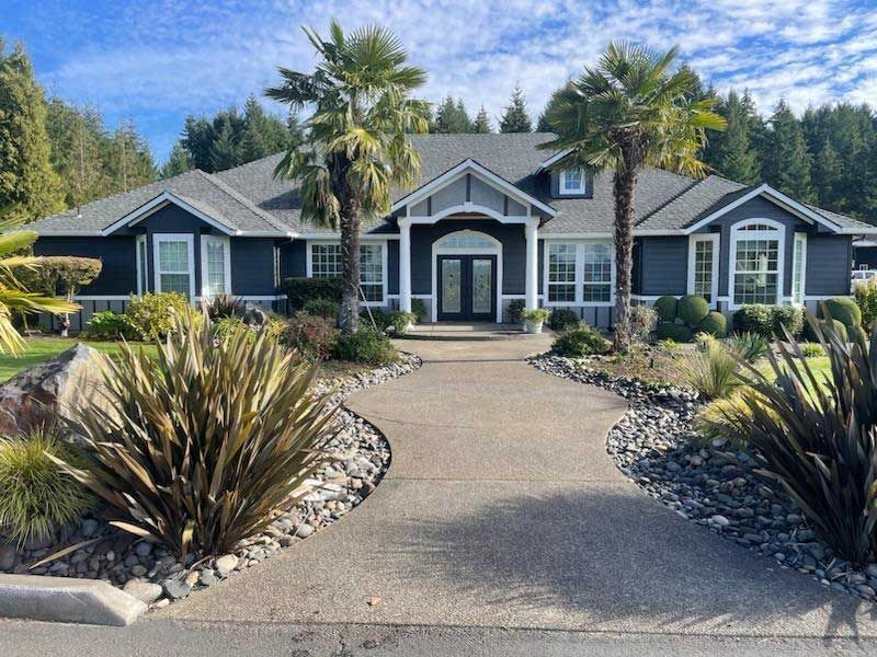 Dark blue house with white trim, palm trees, and a curved walkway.