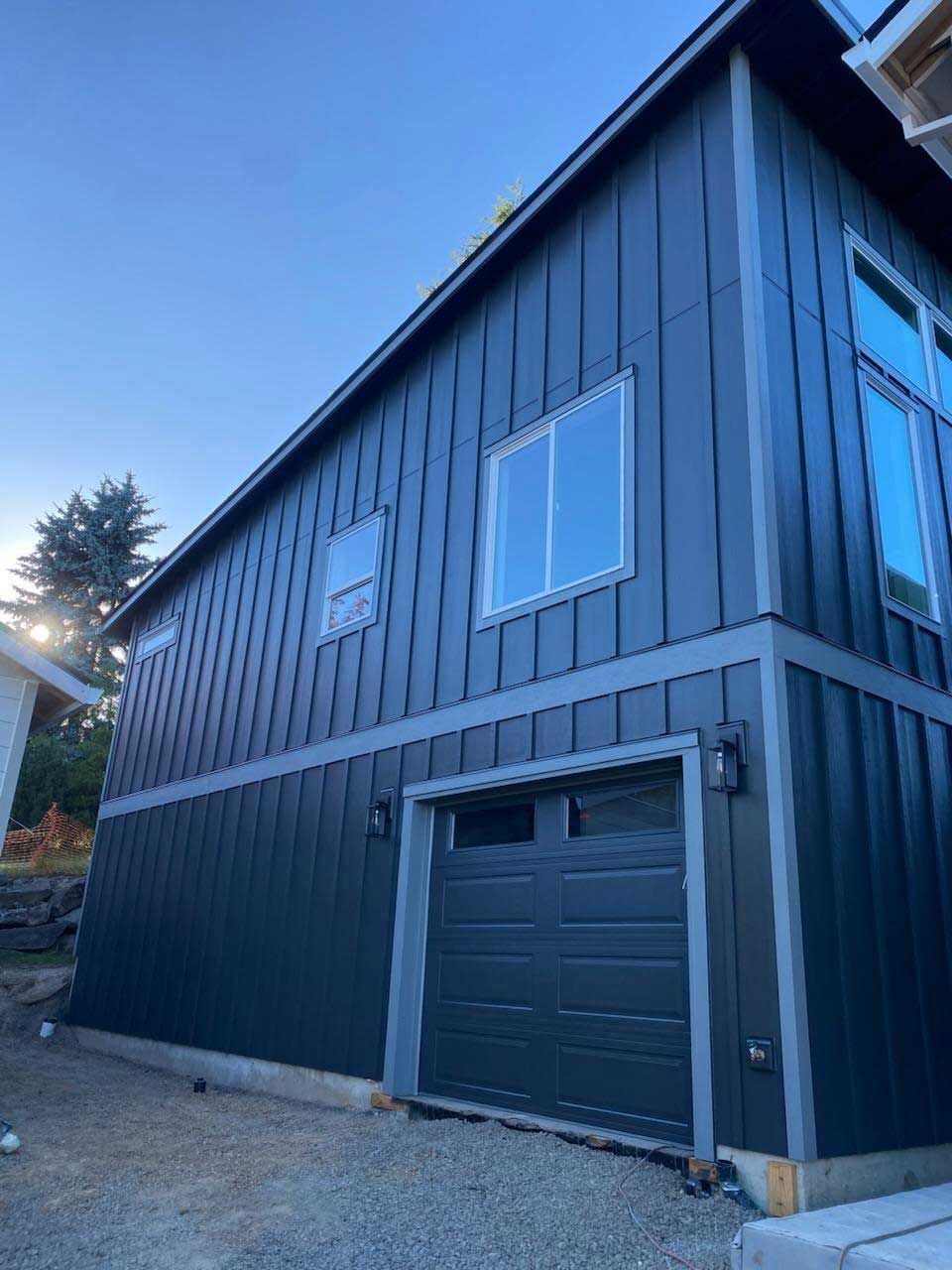 Dark blue modern house with vertical siding, gray trim, garage door, and windows.