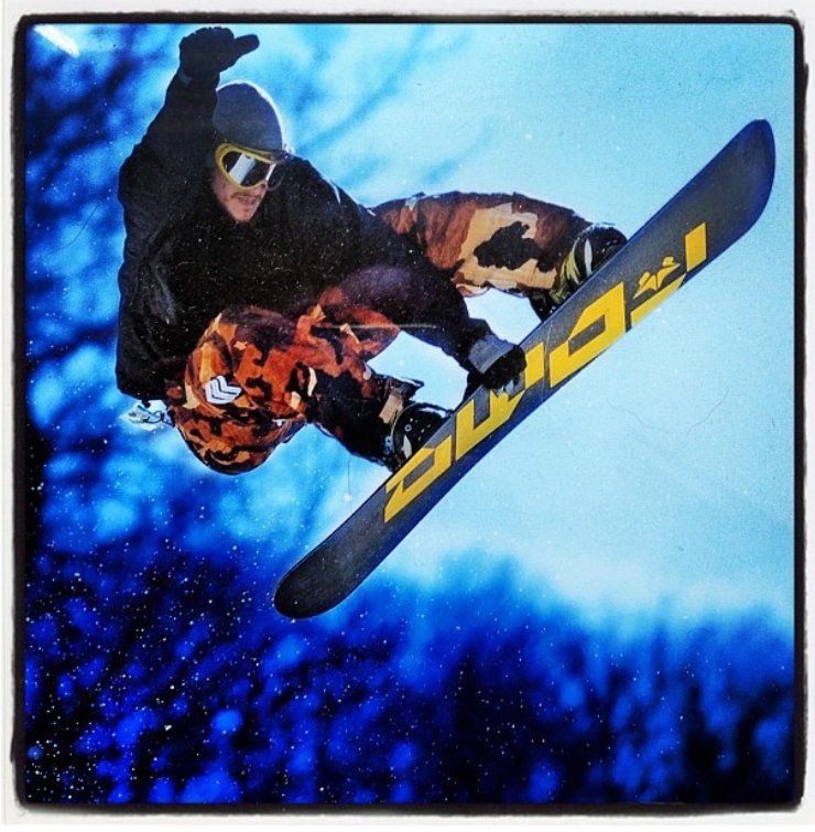 A snowboarder is doing a trick on a board that says ' duca ' on it