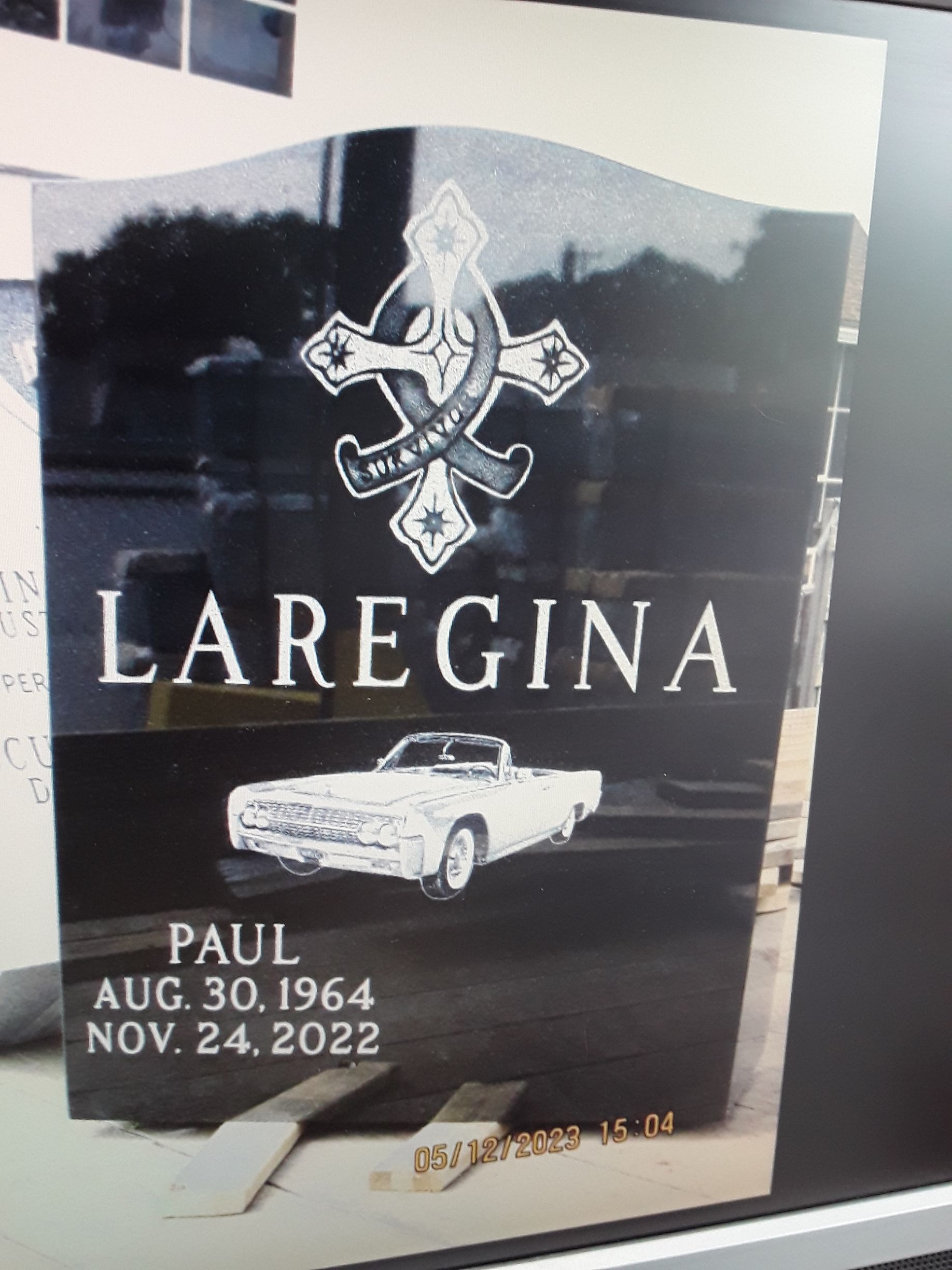 Memorial plaque for Laregina with cross emblem, white car, and dates: Paul, Aug. 30, 1964–Nov. 24, 2022
