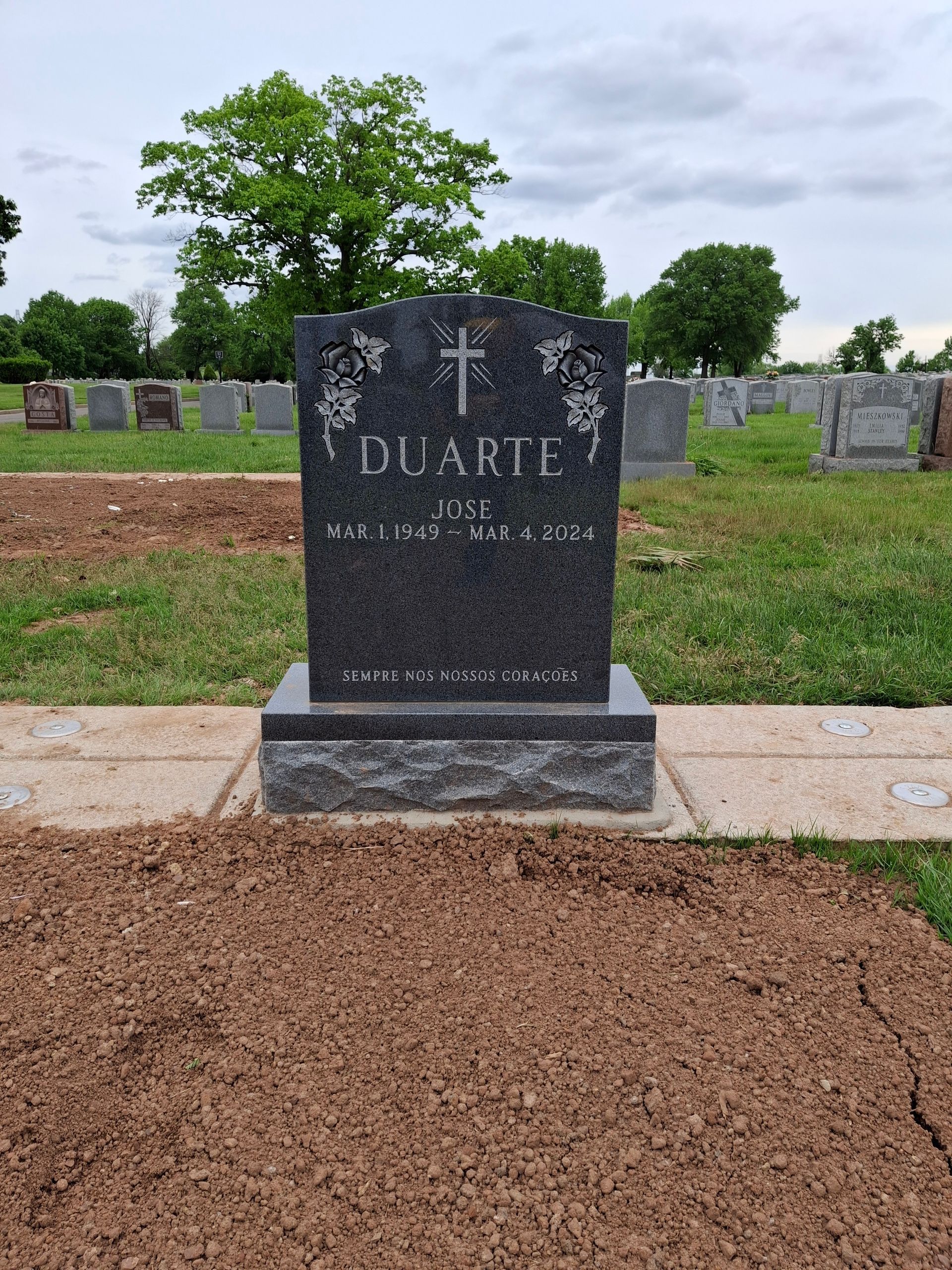Black granite gravestone in a cemetery, with grass, mulch, and trees in the background.