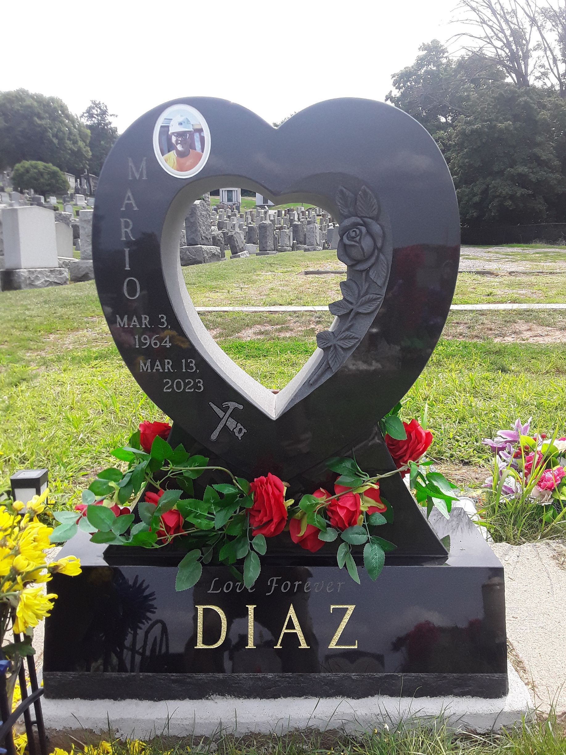 Heart-shaped black memorial with flowers and “DIAZ” engraved on the base in a cemetery