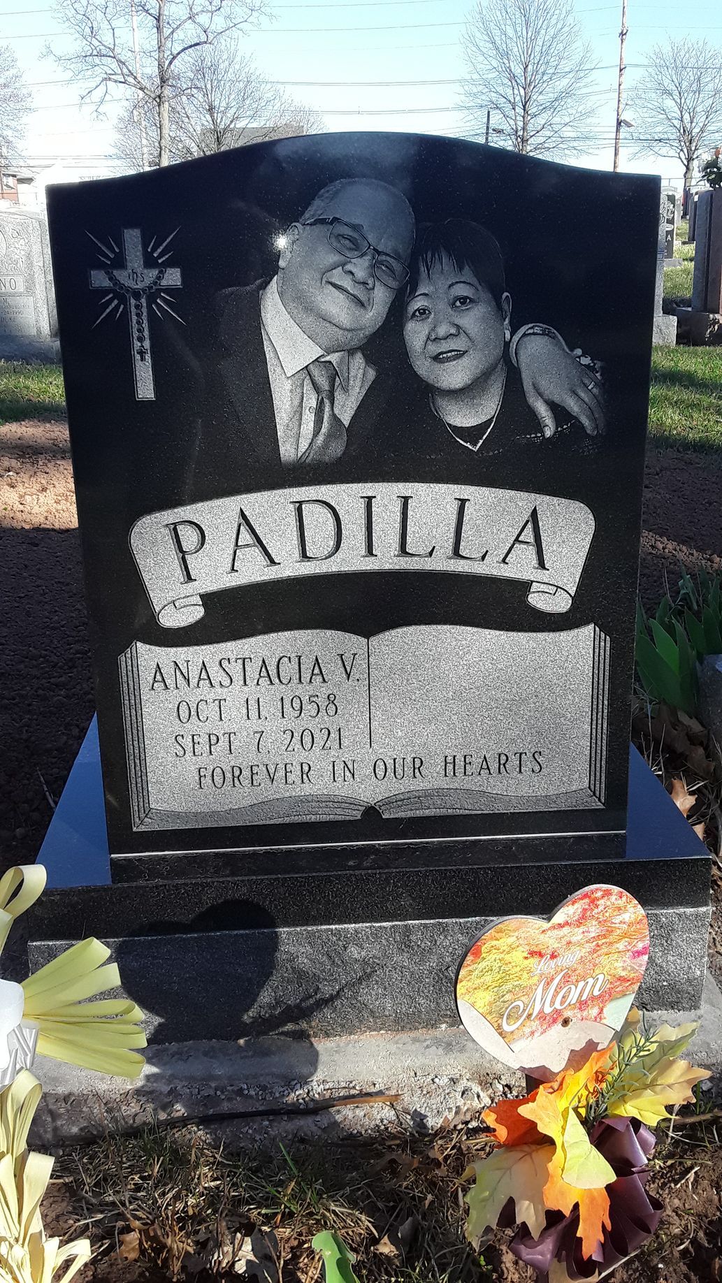 Black gravestone with engraved portraits, “PADILLA,” and flowers at the base.