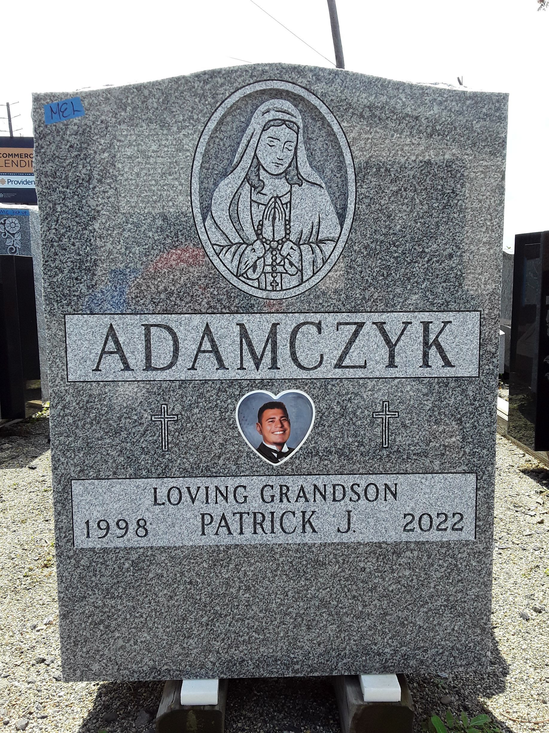 Gray granite gravestone engraved “ADAMCZYK” with a small portrait medallion and dates below