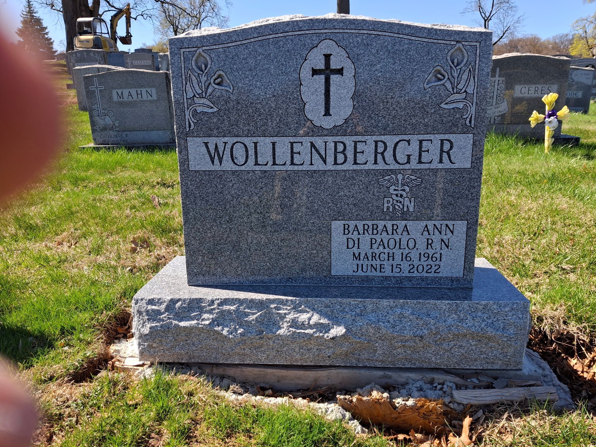 Gravestone marked “Wollenberger” with a cross, set on a grassy cemetery lawn.
