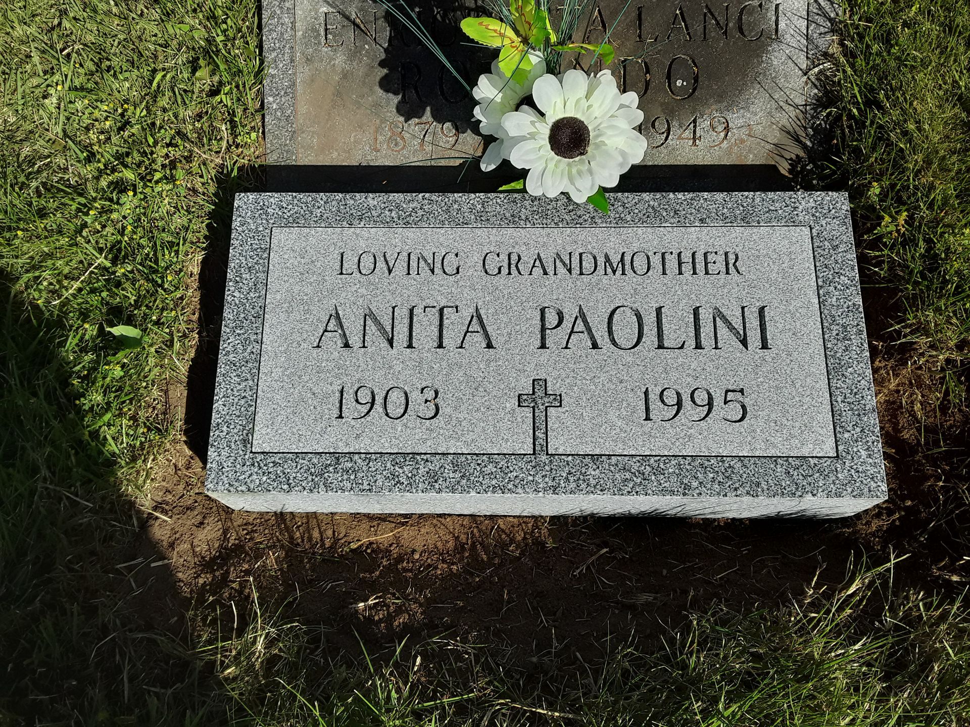 Gravestone for Anita Paliuk, 1903–1995, with white flowers on top.