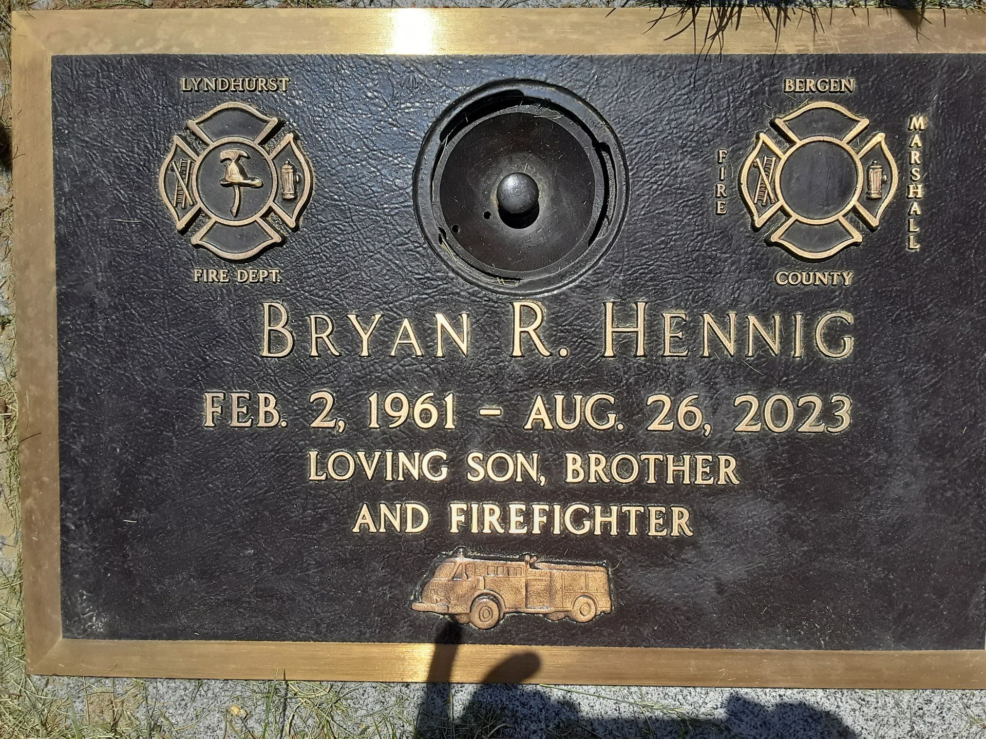 Bronze memorial plaque for Bryan R. Hennig with fire service emblems and dates Feb. 2, 1961–Aug. 26, 2023