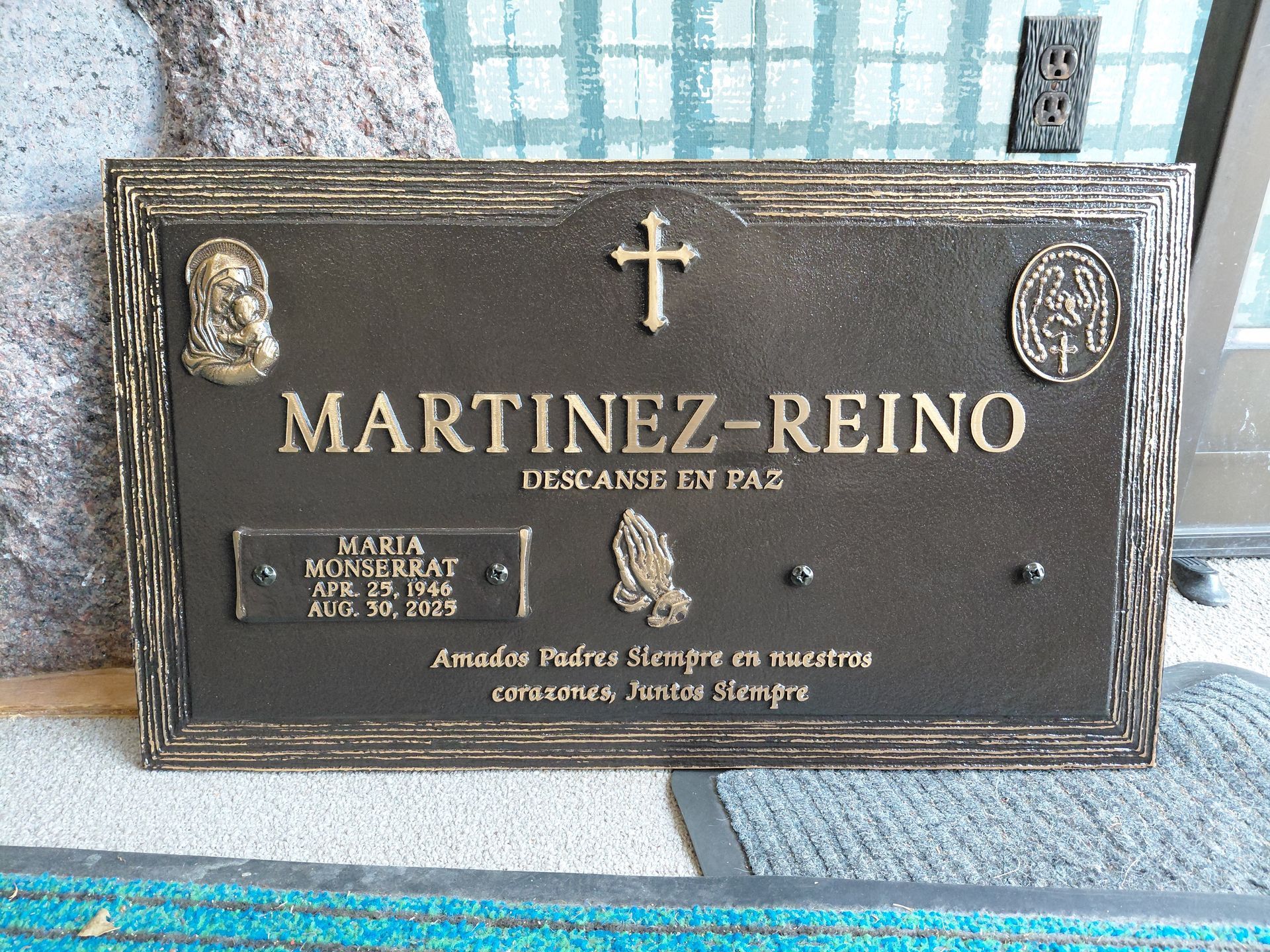 Black granite memorial plaque with gold text and cross, reading “MARTINEZ-REINO” on a stone wall.