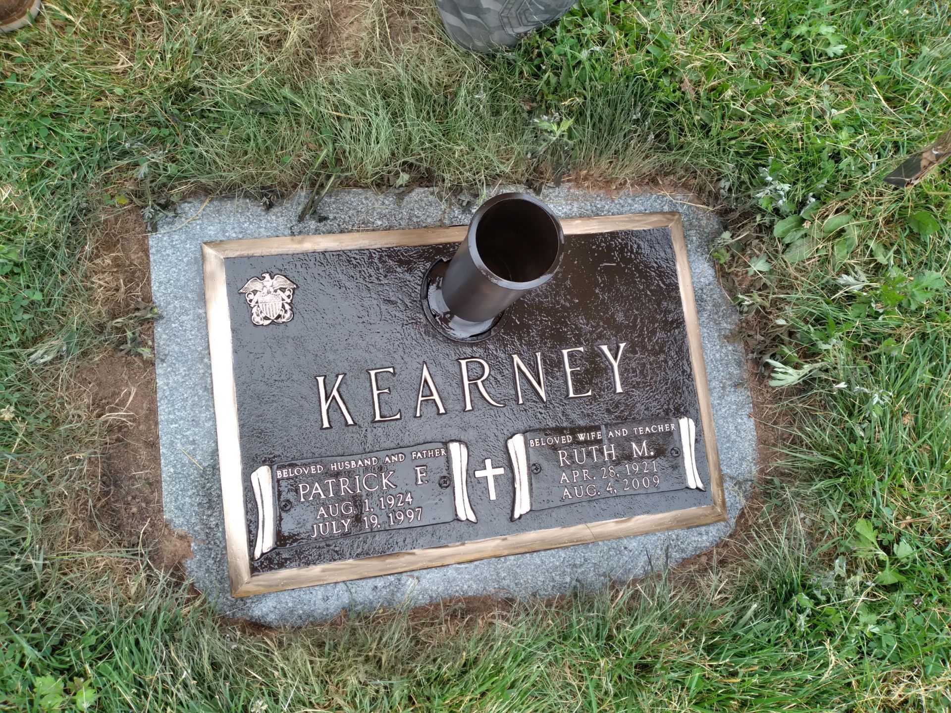 Bronze grave marker for Kearney set in grass, with a small pipe-like vase.