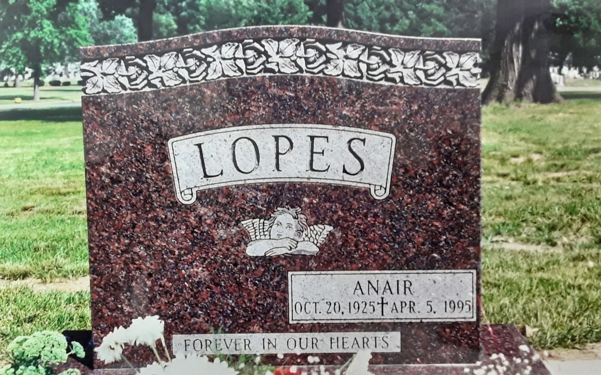 Maroon granite Lopez family gravestone in a grassy cemetery with trees in the background