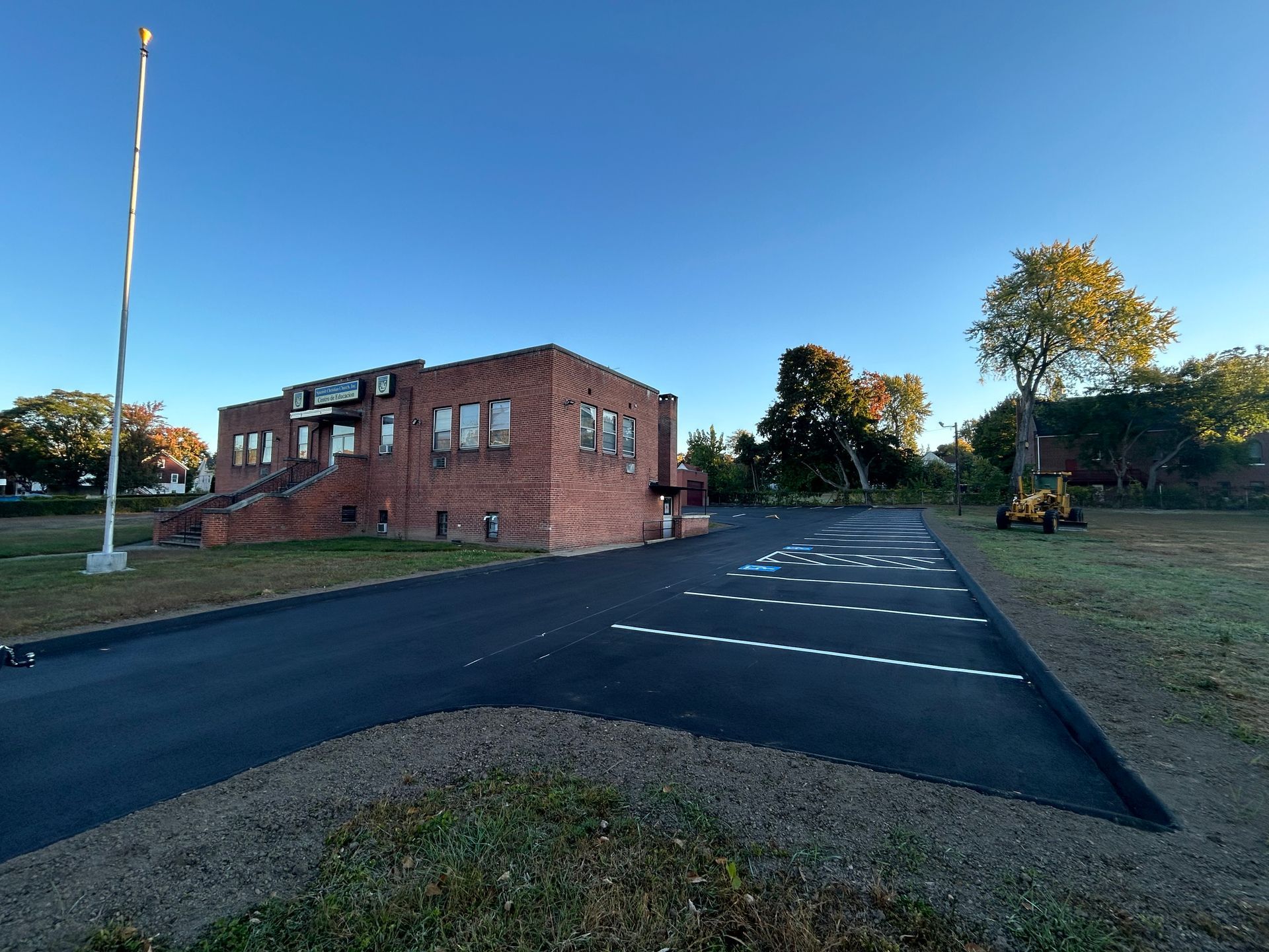 Brick building with a parking lot featuring a painted accessible parking symbol on a sunny day.