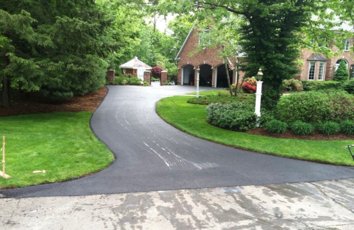 A fresh, black asphalt driveway curves through a lush green lawn leading to a brick garage and house.