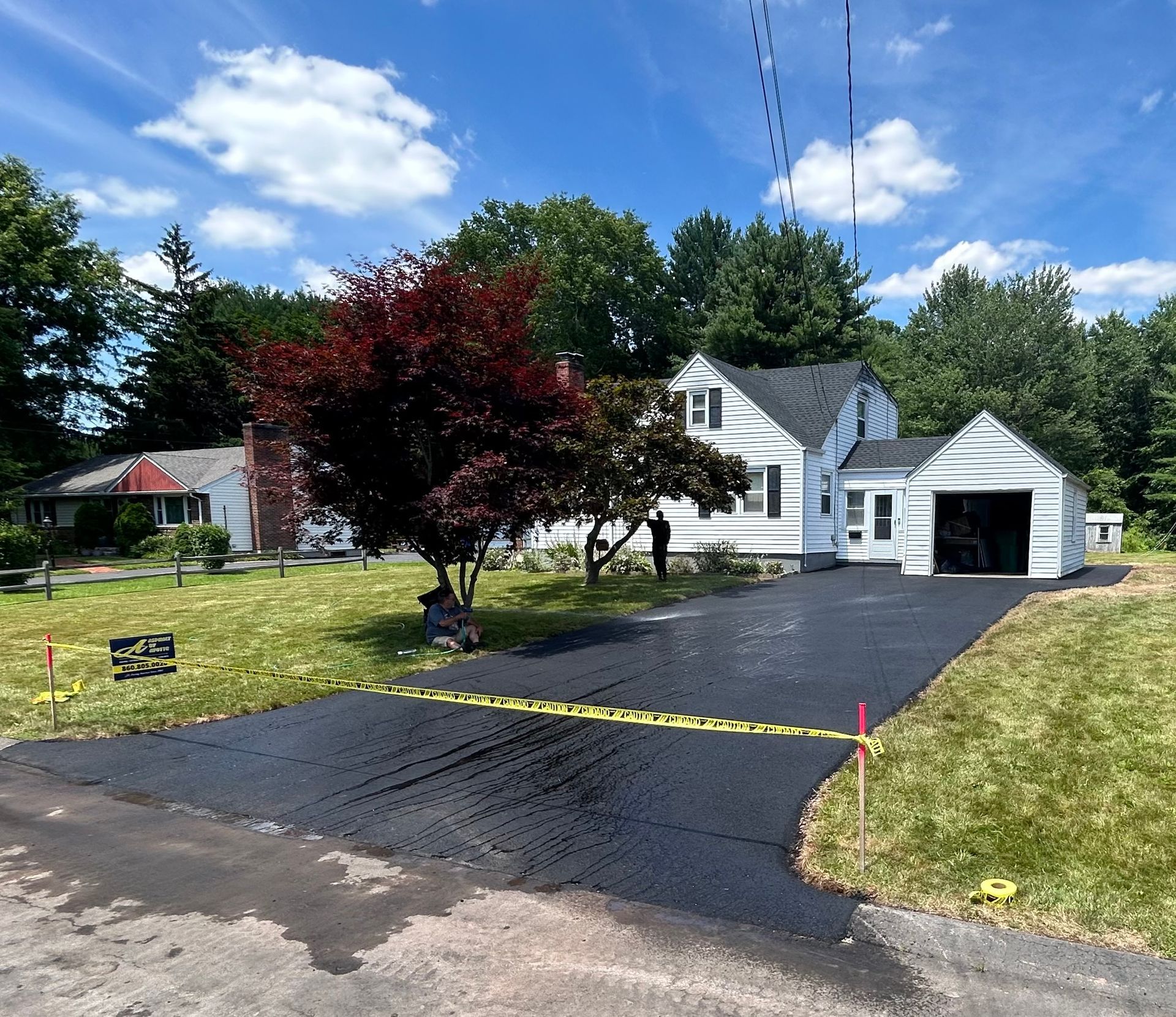 A newly paved black asphalt driveway leading to a white suburban home on a sunny day.