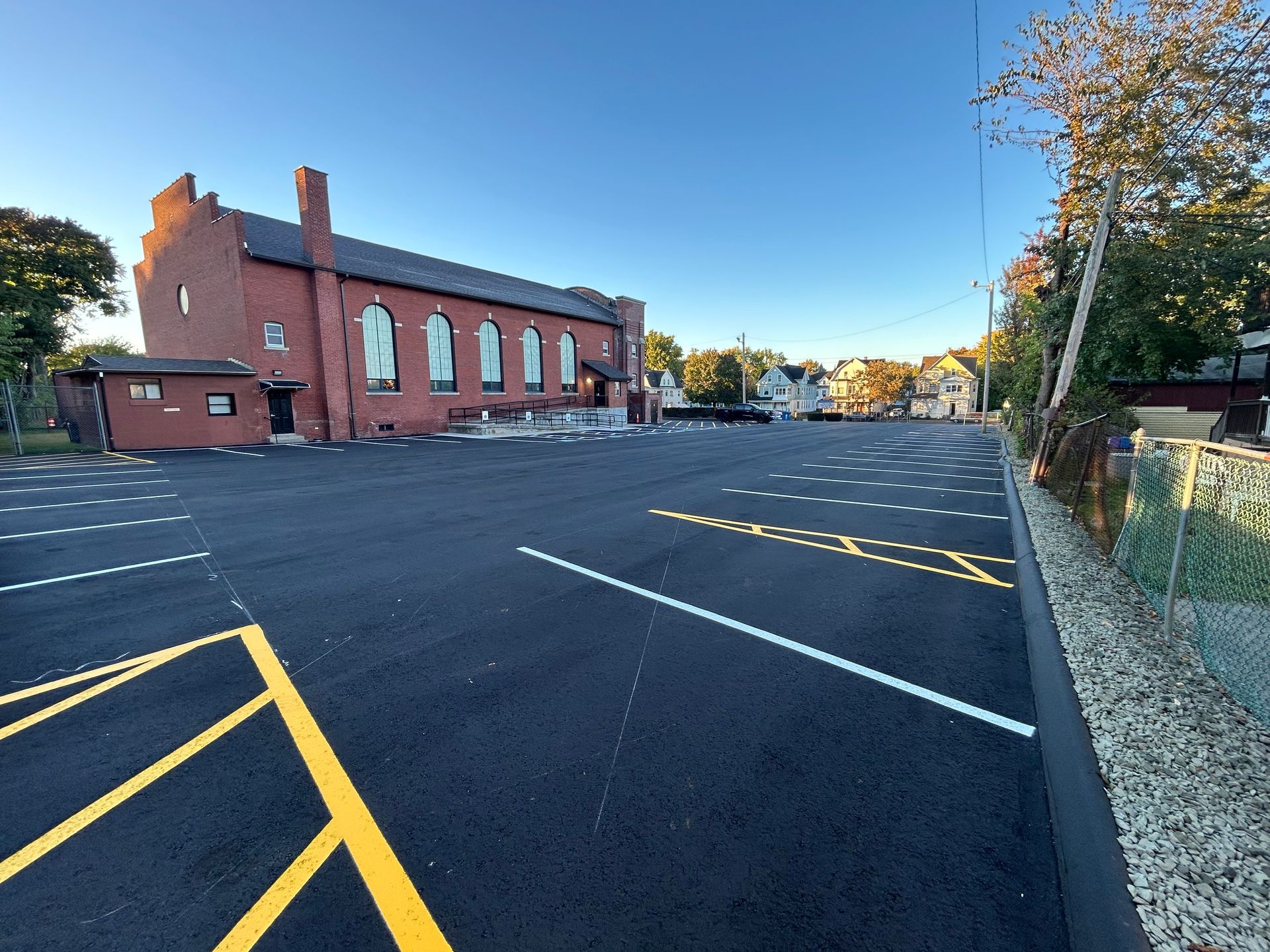 A newly paved parking lot beside a red brick building with arched windows under a clear blue sky.
