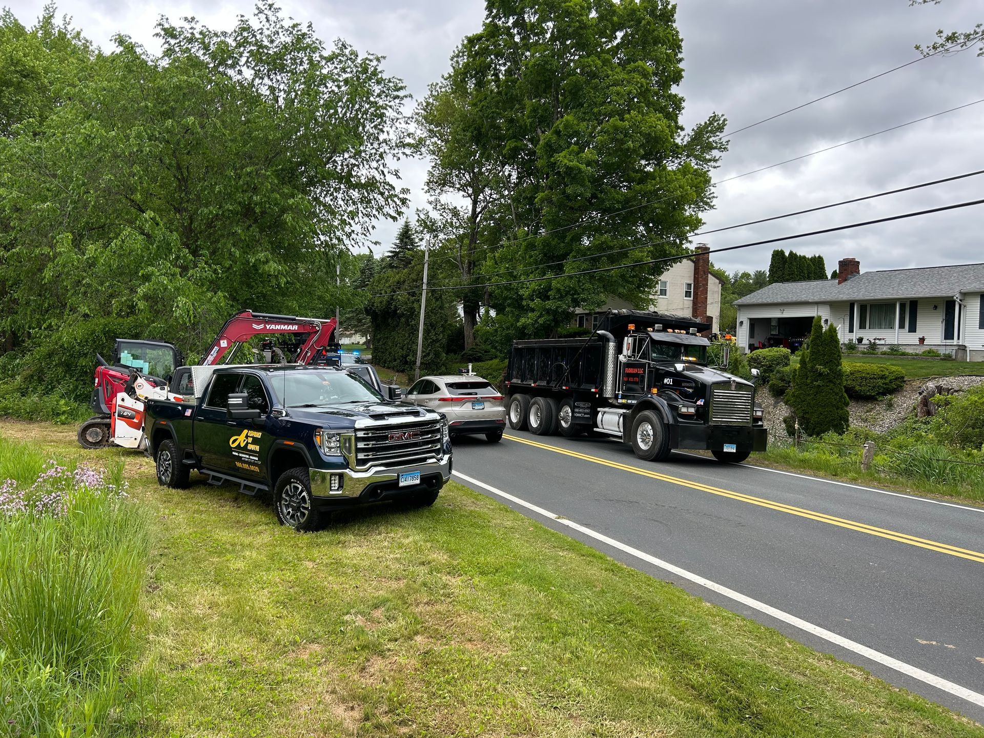 A dark pickup truck and a black dump truck parked on the side of a rural road near a piece of construction machinery.