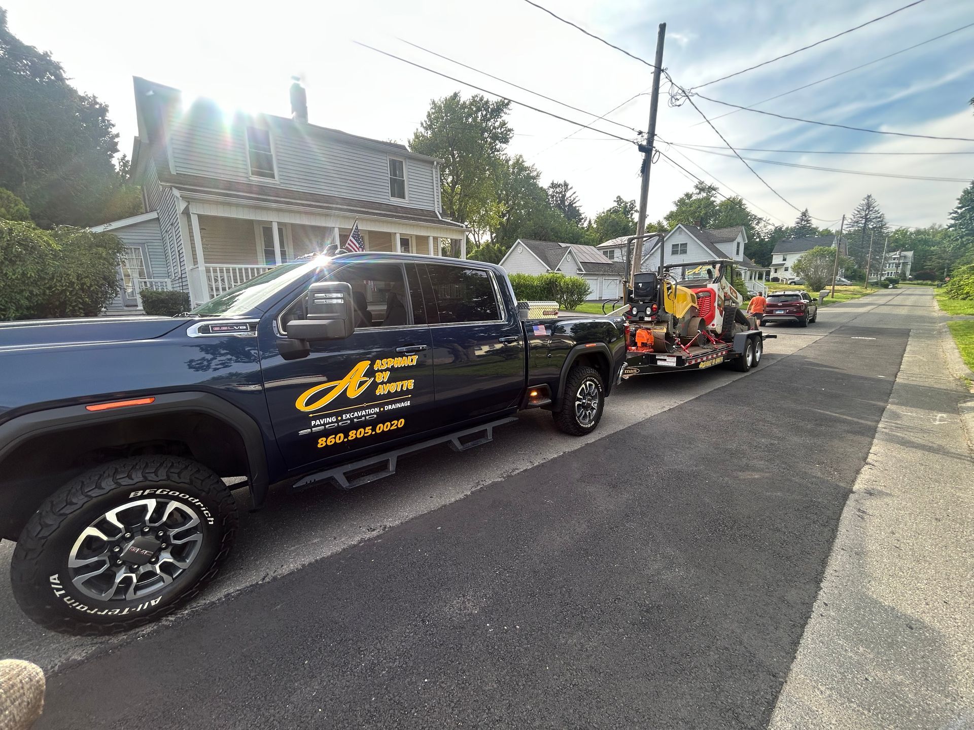 A dark blue pickup truck towing a trailer with equipment parked on a residential street.