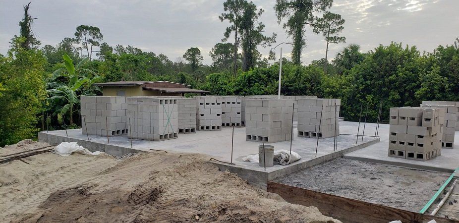 A house is being built in the middle of a dirt field with trees in the background.