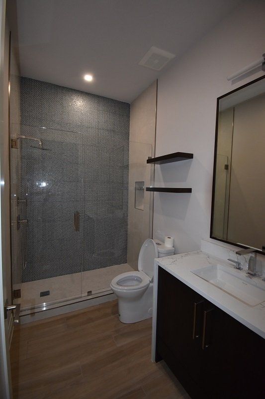 A bathroom with a toilet, sink, mirror and walk in shower.