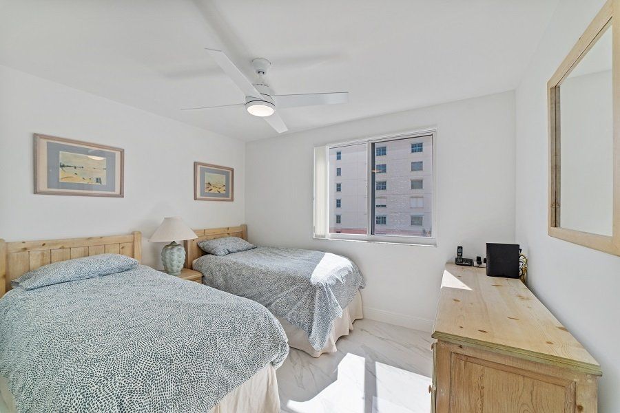 A bedroom with two beds, a dresser, a mirror and a ceiling fan.
