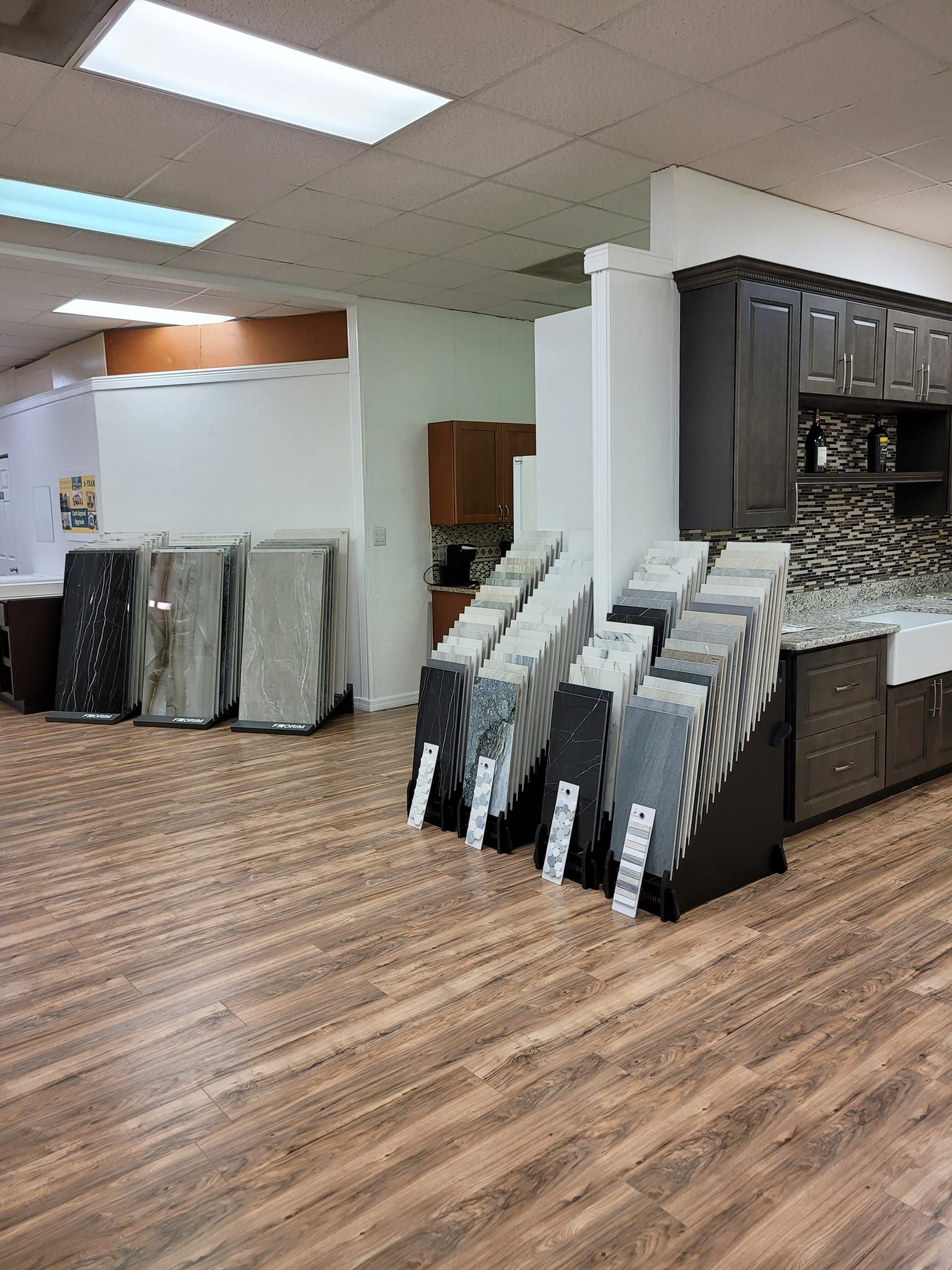 Showroom with granite countertop samples and kitchen cabinets, wood-look flooring.