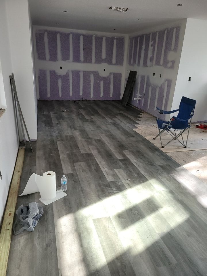 Room under construction with gray plank flooring, drywall walls, and a folding chair.